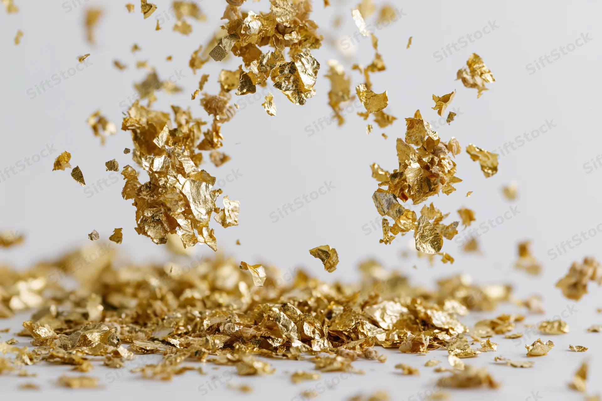 Gold metallic confetti pieces falling and scattering midair on white surface