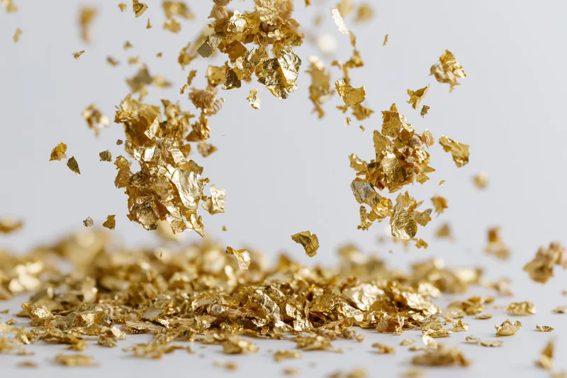 Gold metallic confetti pieces falling and scattering midair on white surface