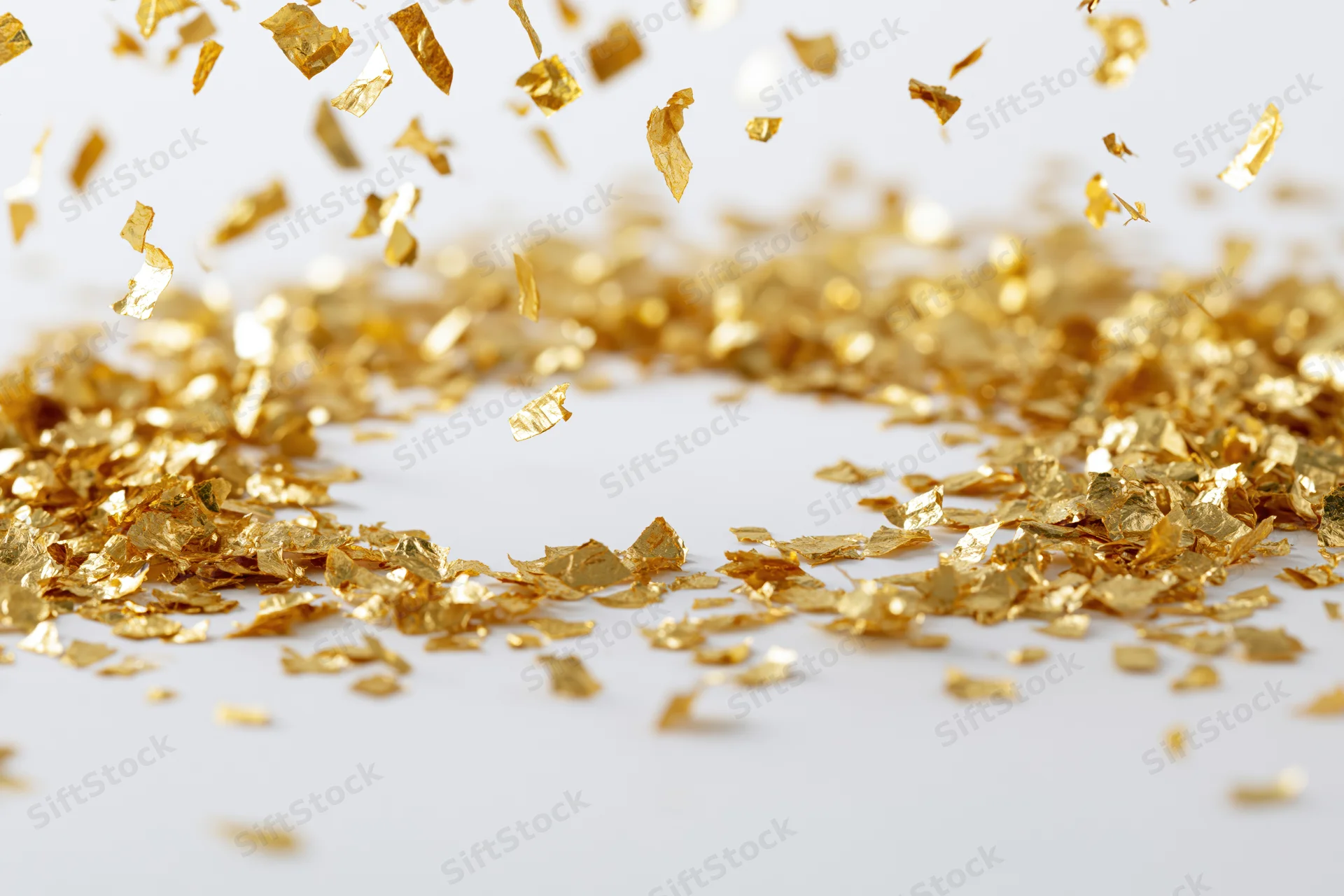 Gold metallic confetti pieces falling and scattering midair on a white surface