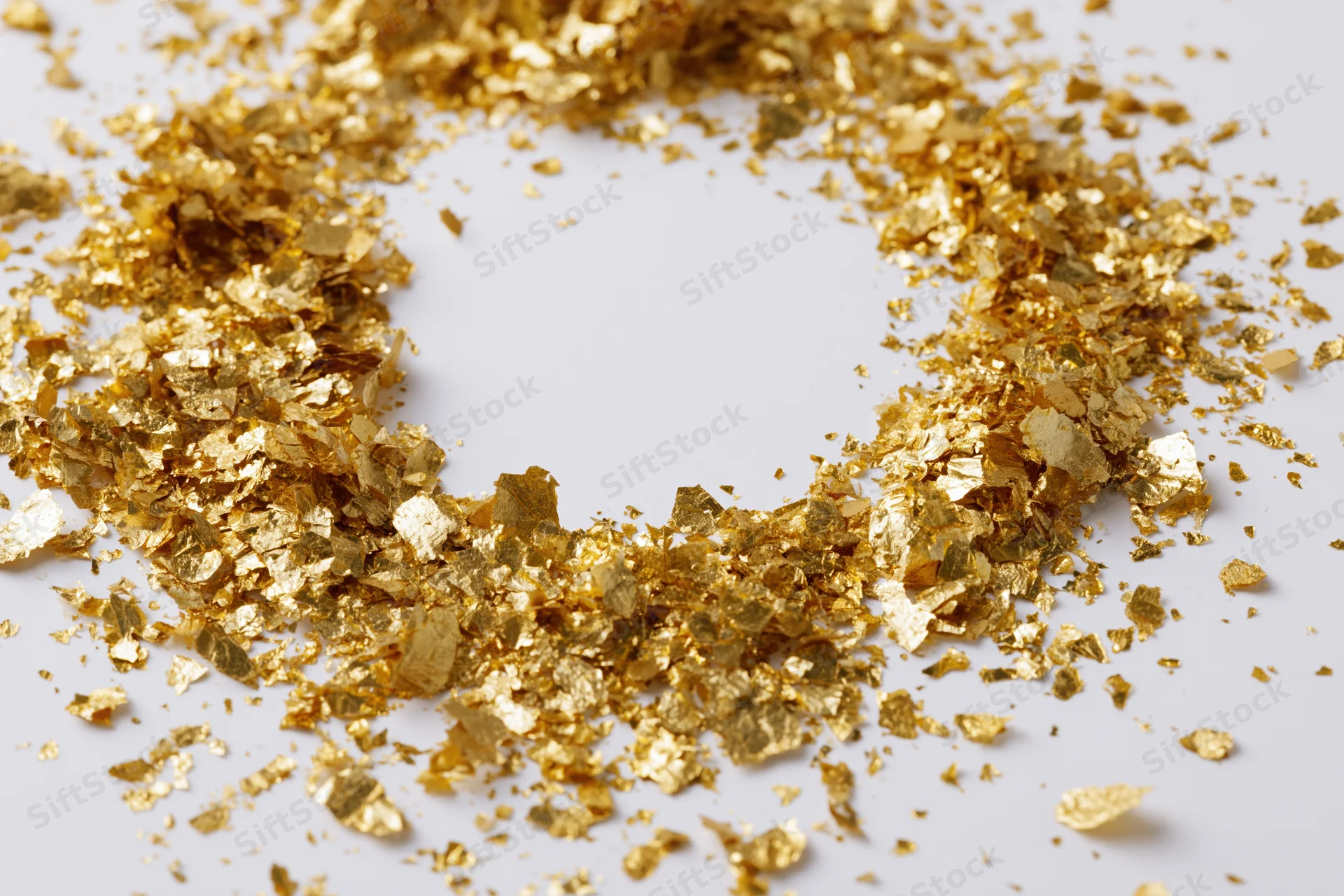 Gold metallic confetti pieces scattered in a circular pattern on a white surface