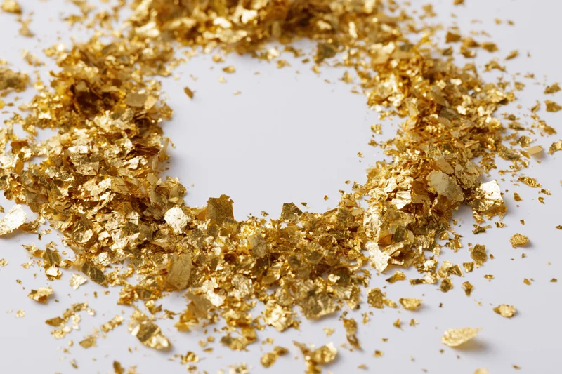Gold metallic confetti pieces scattered in a circular pattern on a white surface