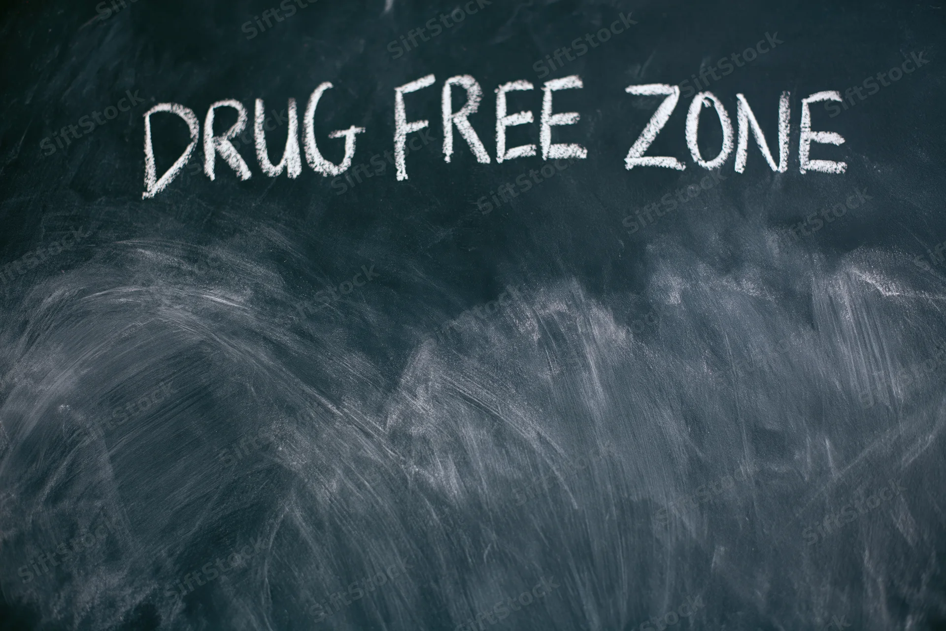 Handwritten chalk text reading drug free zone on a dark blackboard surface