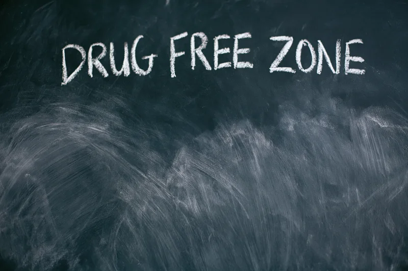 Handwritten chalk text reading drug free zone on a dark blackboard surface