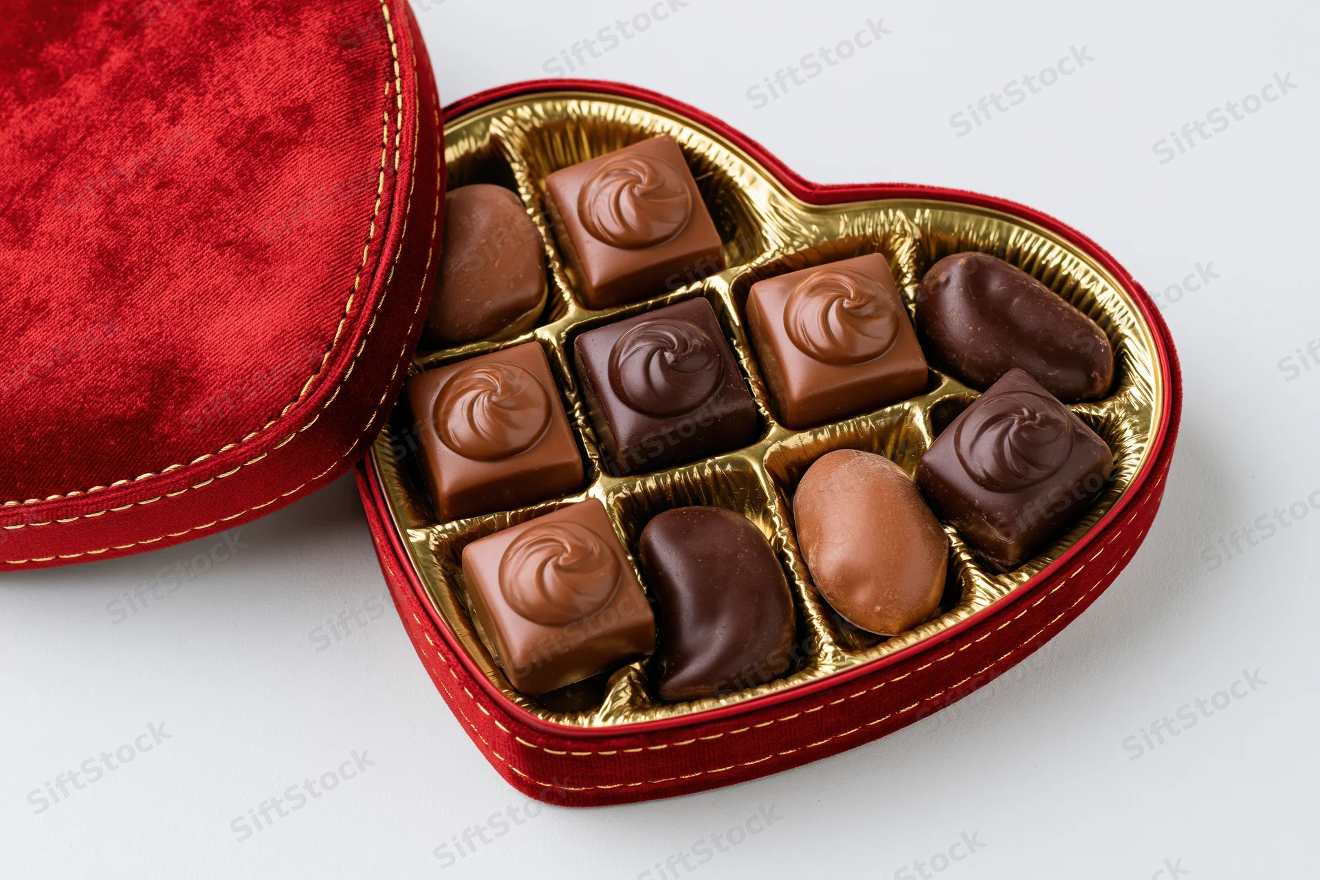 Heart-shaped chocolate gift box open on white background showing assorted chocolates in gold tray with red velvet lid