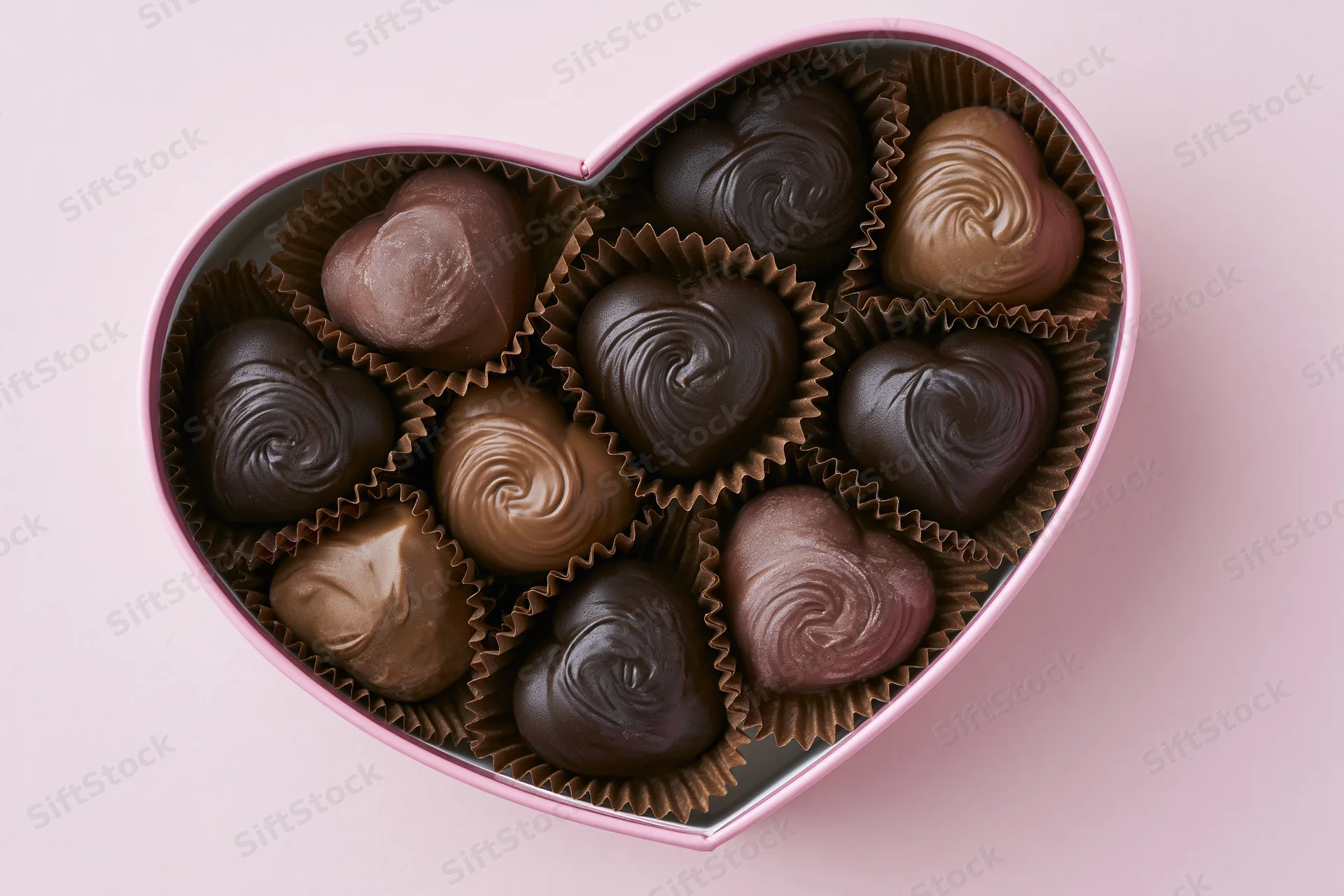 Heart-shaped box filled with assorted chocolates on pink background