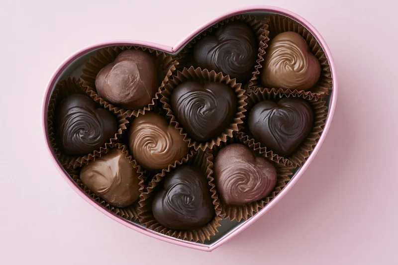 Heart-shaped box filled with assorted chocolates on pink background