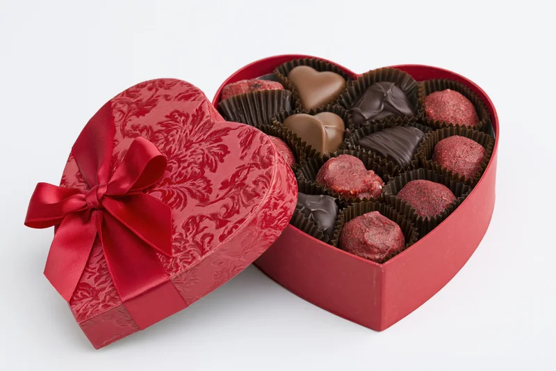 Heart-shaped red gift box filled with assorted milk and dark chocolates on white background