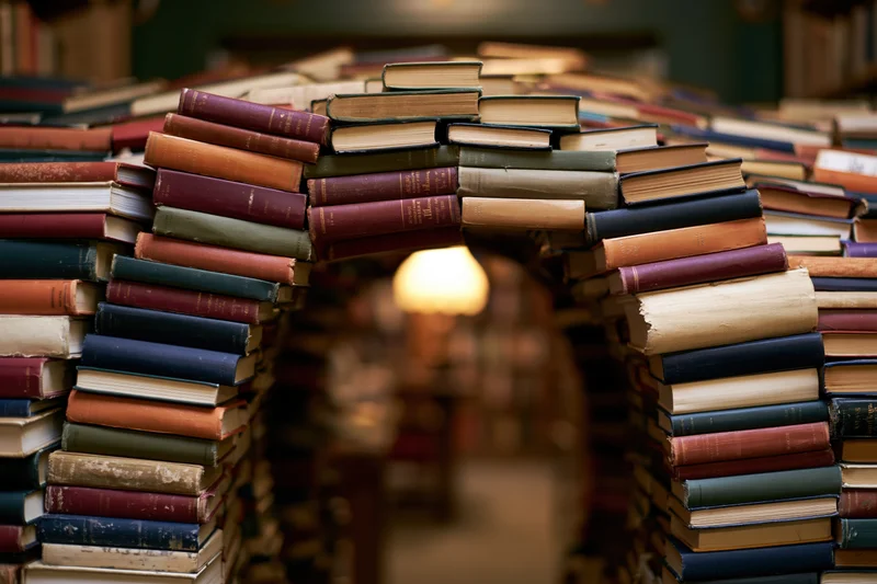 Stacks of vintage books forming an archway tunnel in a library interior
