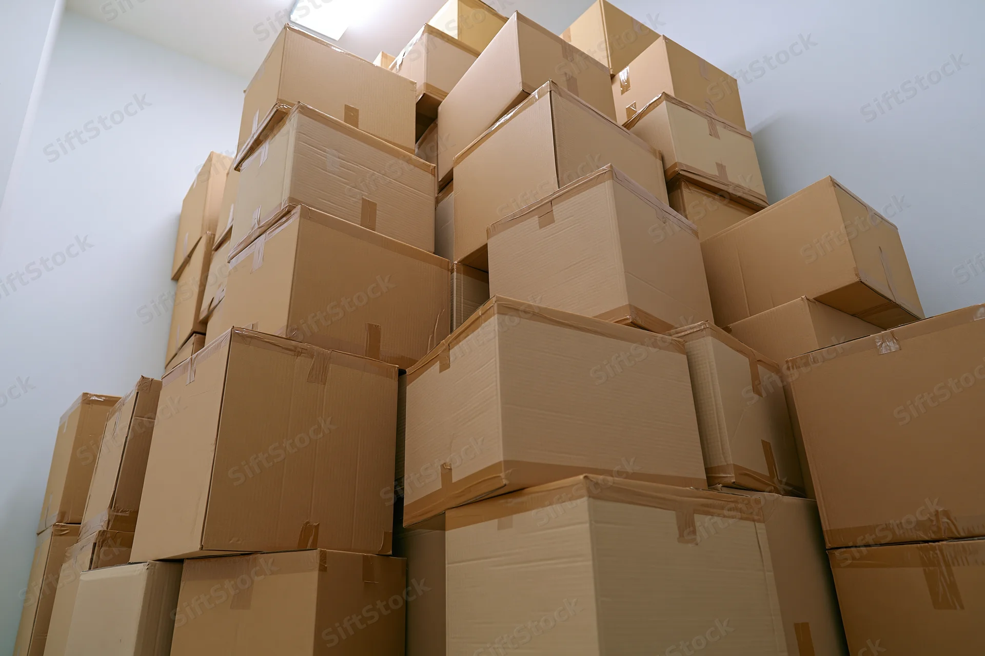 Stacked cardboard boxes filling a white room from low angle view