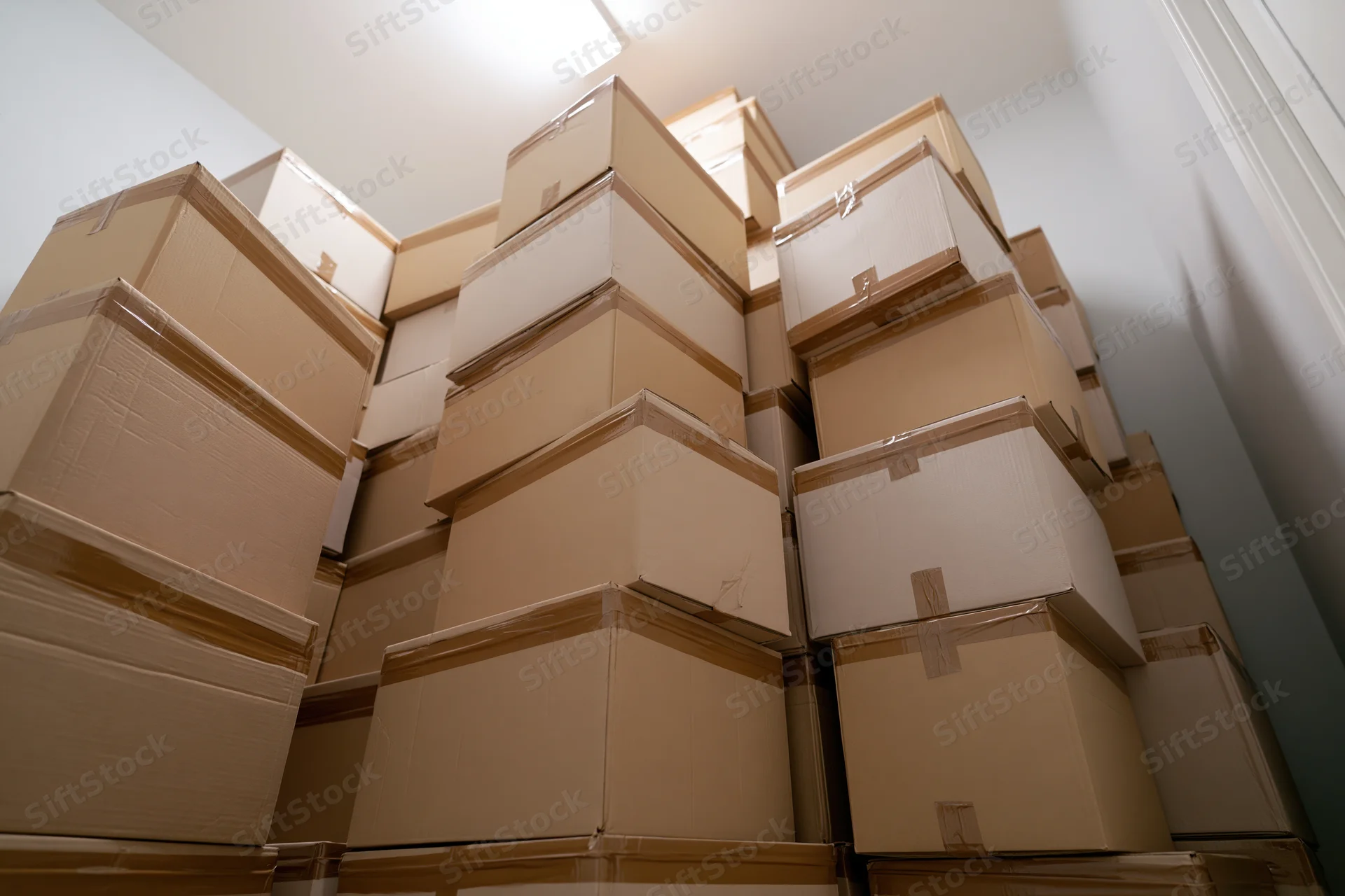 Stacked cardboard boxes filling a white room under fluorescent ceiling light