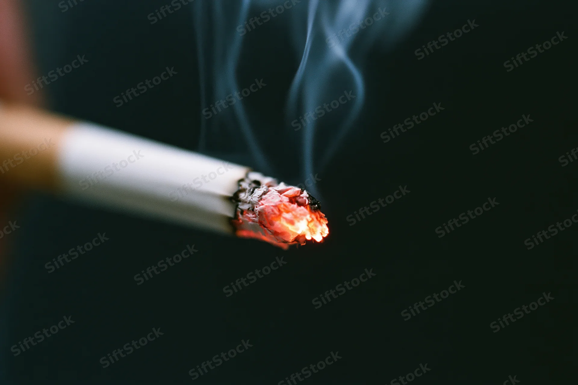 Closeup of a lit cigarette burning with smoke against a black background