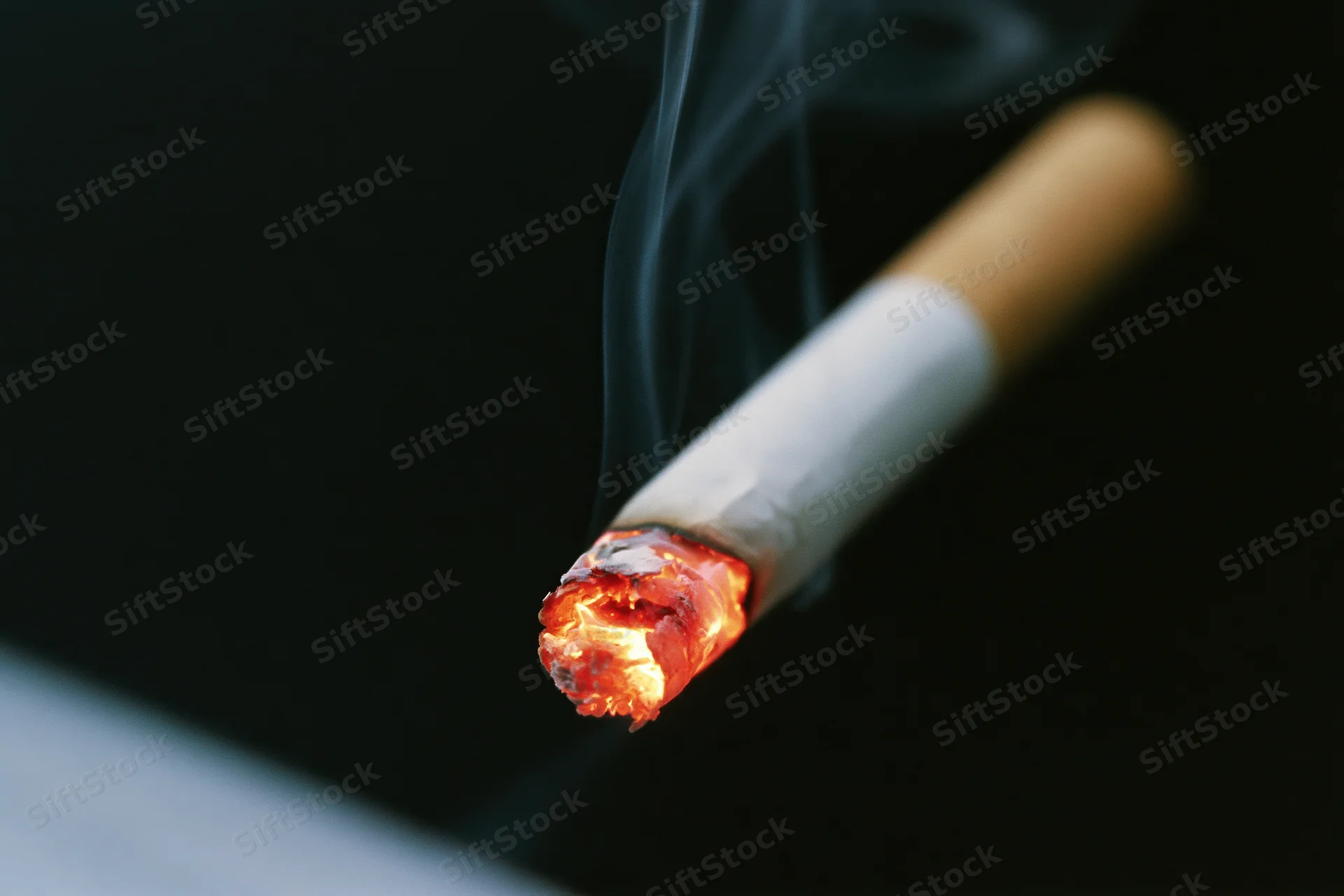 Lit cigarette burning with glowing ember and rising smoke against black background