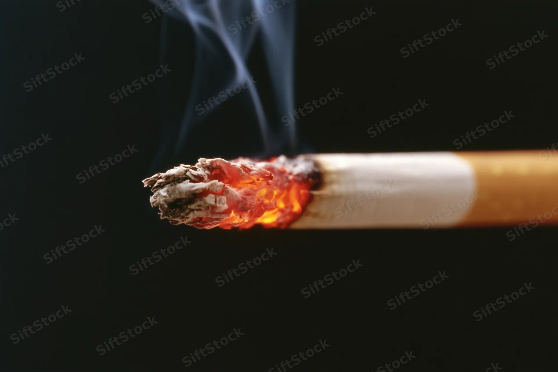 Lit cigarette burning with glowing ember and rising smoke against black background