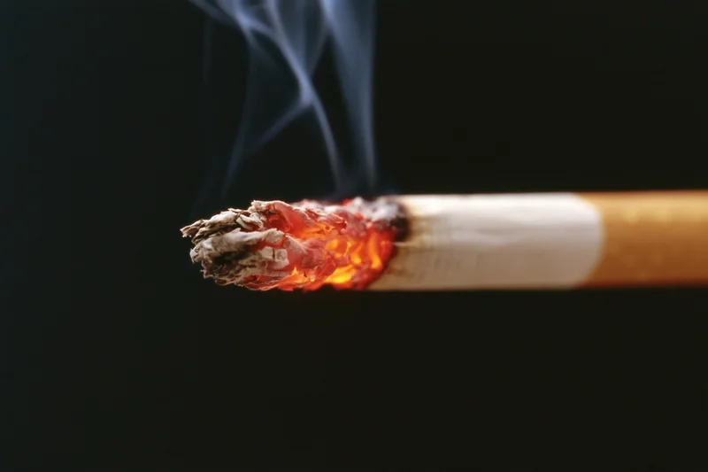Lit cigarette burning with glowing ember and rising smoke against black background