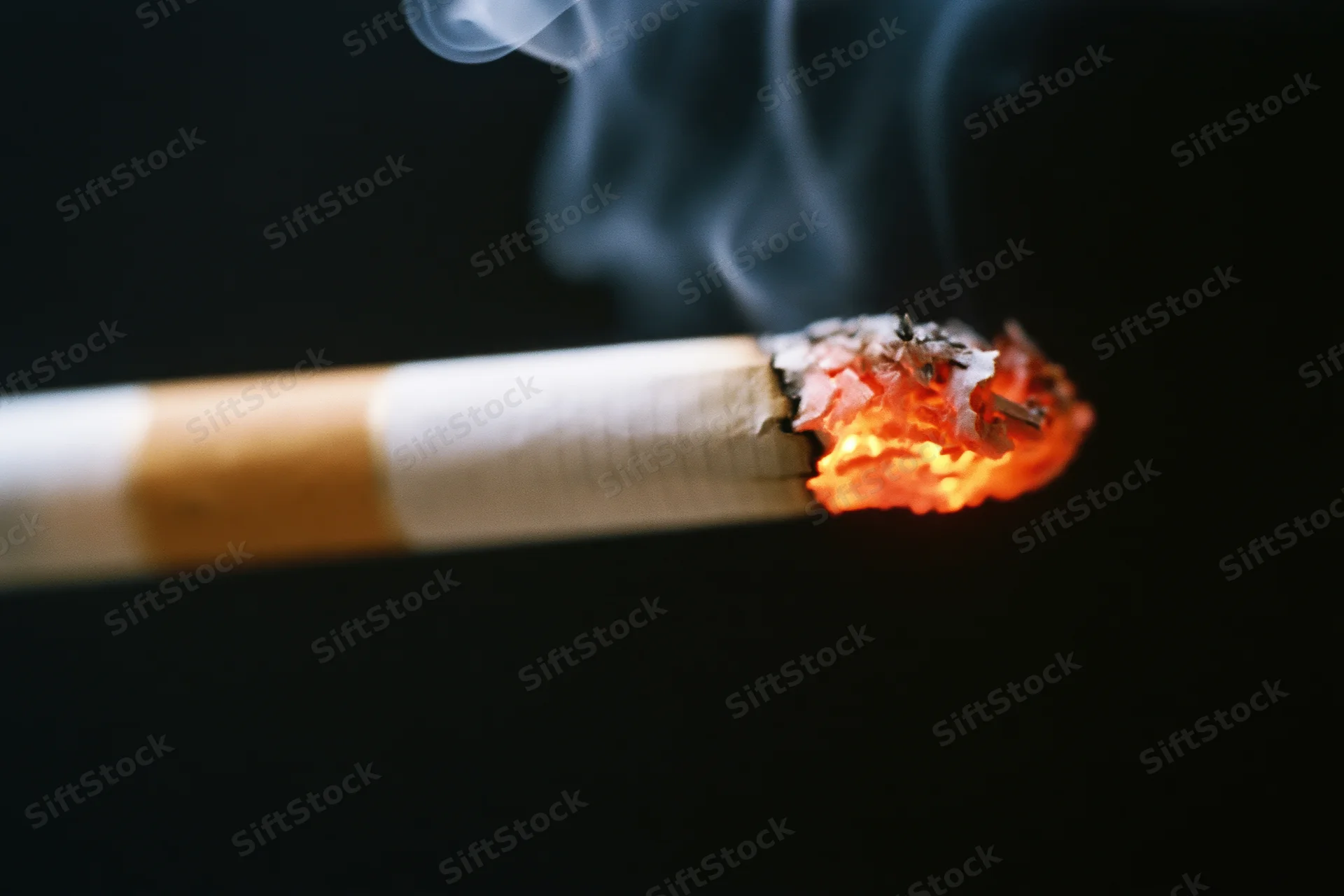 Lit cigarette burning with glowing ember and rising smoke against black background