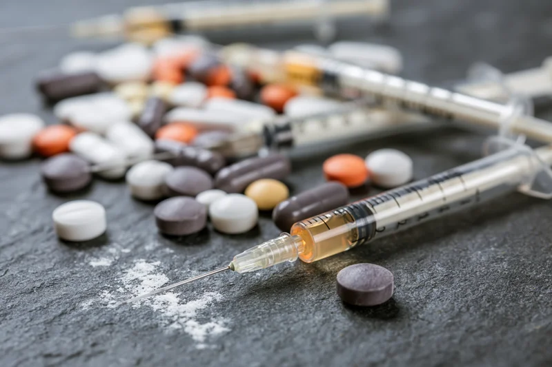 Syringes and assorted pills scattered on dark slate surface