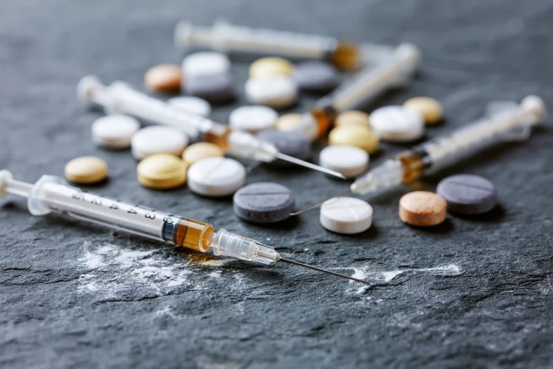 Syringes and pills scattered on dark slate surface