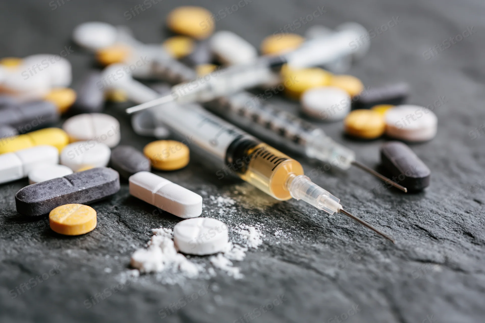 Syringes and assorted pills scattered on dark slate surface