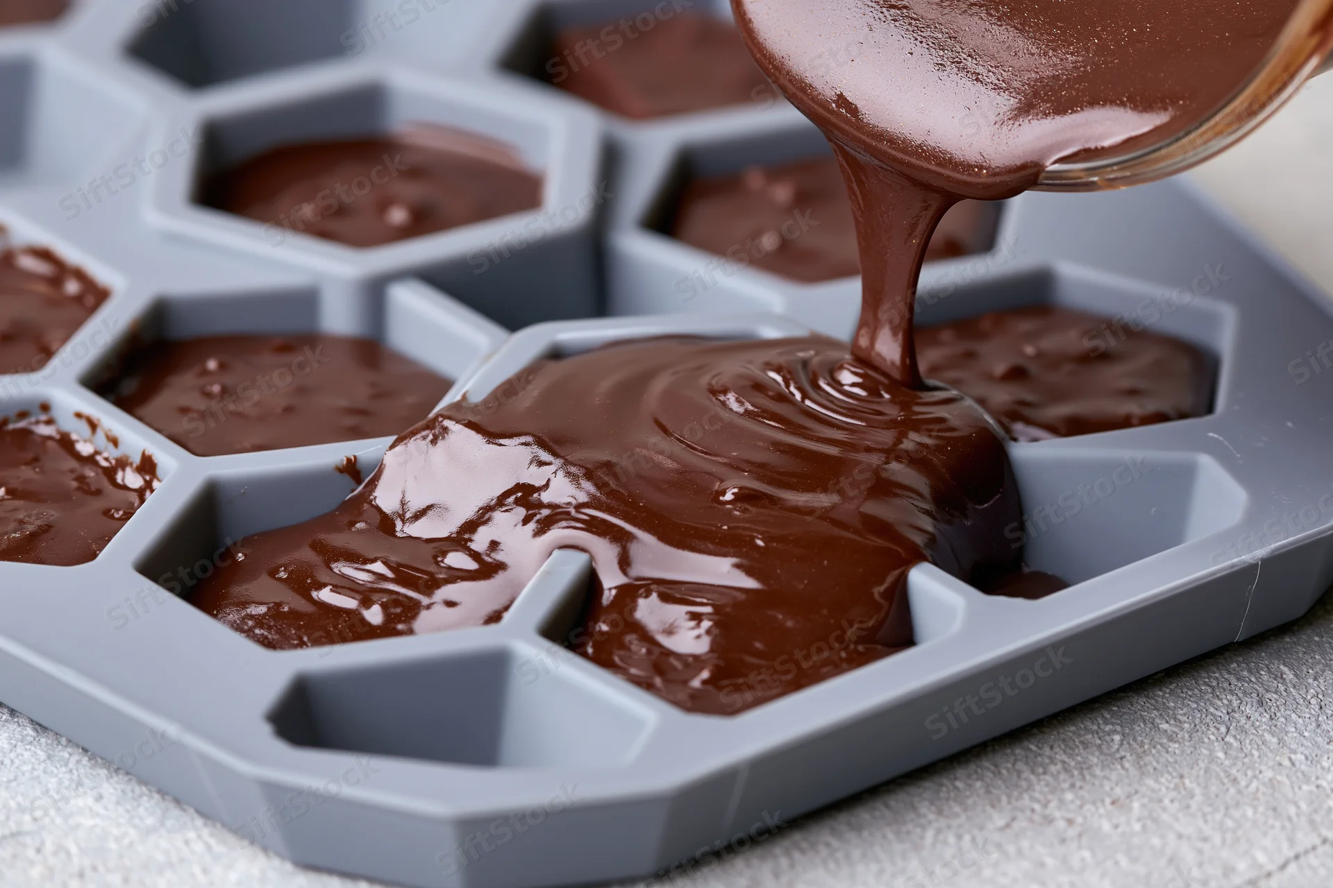 Melted dark chocolate being poured into a hexagonal silicone mold for baking