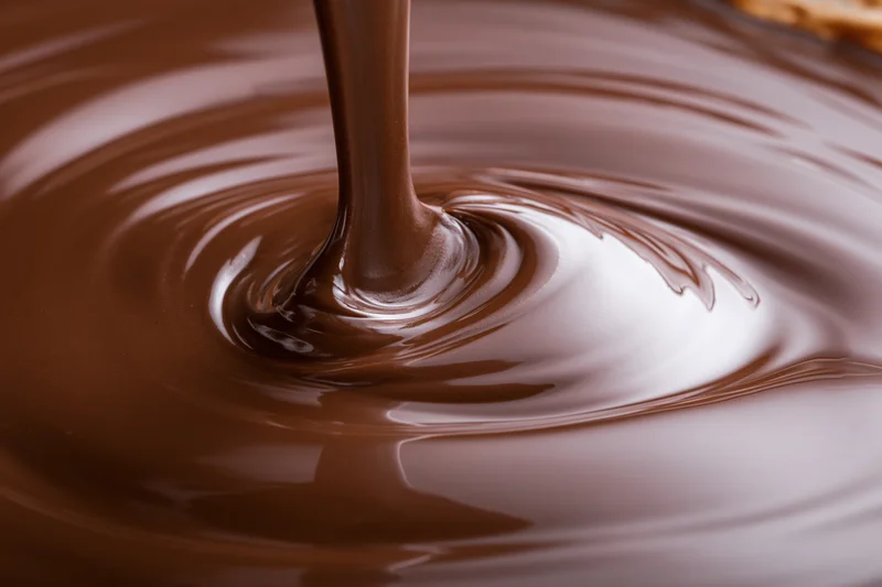 Dark chocolate pouring in a slow stream creating ripples on a glossy surface