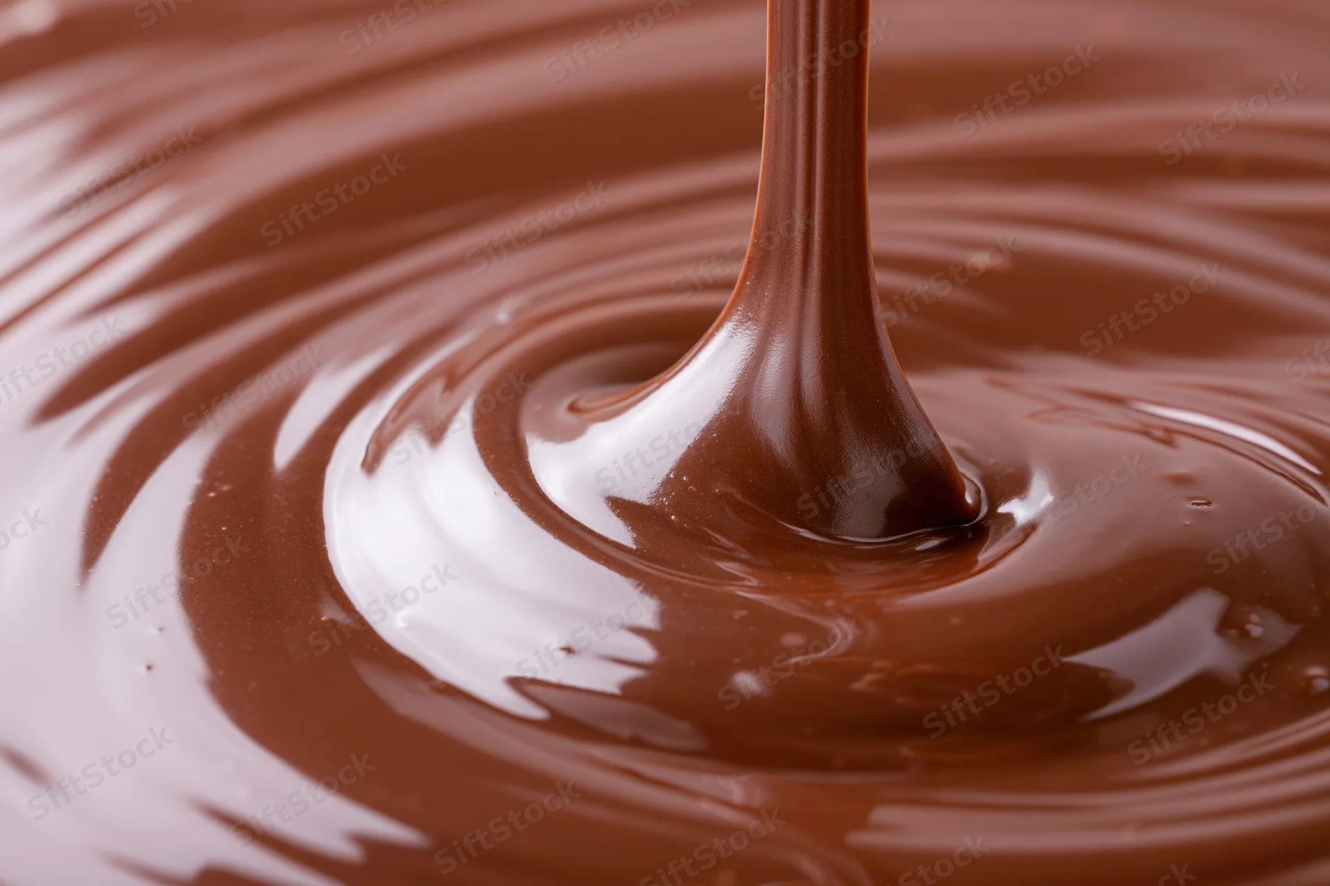 Melted dark chocolate pouring in a slow stream creating ripples and swirls on a glossy surface