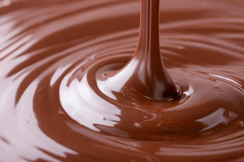 Melted dark chocolate pouring in a slow stream creating ripples and swirls on a glossy surface