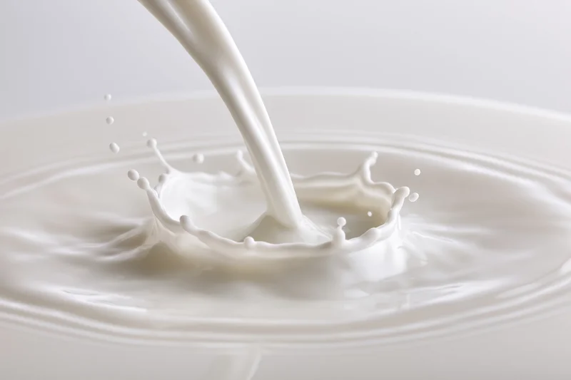Milk being poured into a shallow pool creating a splash and ripples on a white surface