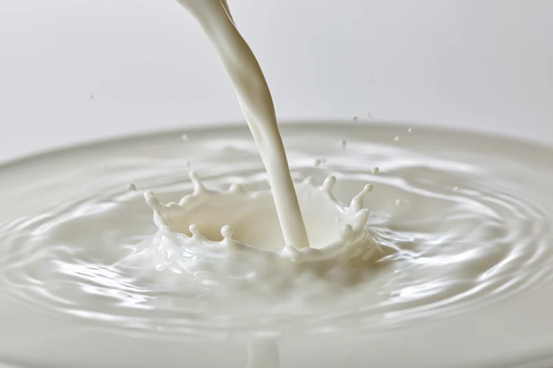 Milk being poured into a shallow pool creating a splash and ripples on a white surface