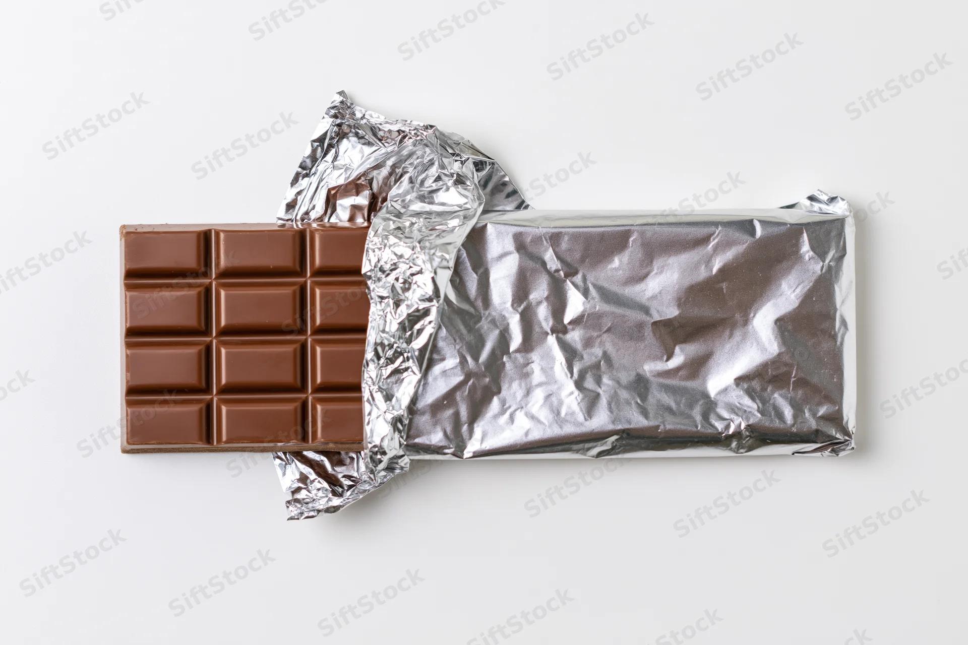 Partially unwrapped milk chocolate bar on white background with crinkled silver foil wrapper