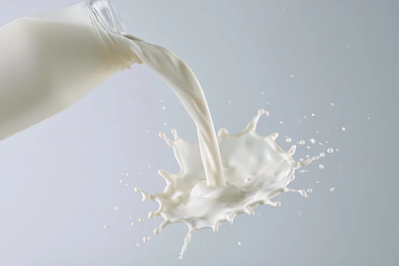 Milk pouring from a glass bottle creating a mid-air splash against a plain background
