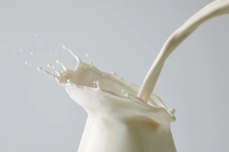 Milk pouring in a steady stream creating a mid-air splash against a plain background