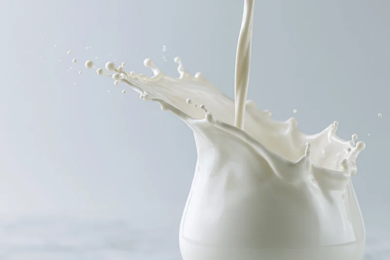 Milk pouring into a glass creating a dynamic splash mid-air against a light background