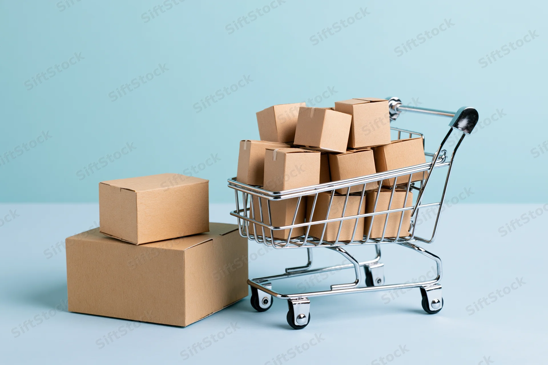 Miniature metal shopping cart filled with small cardboard boxes on a light blue surface