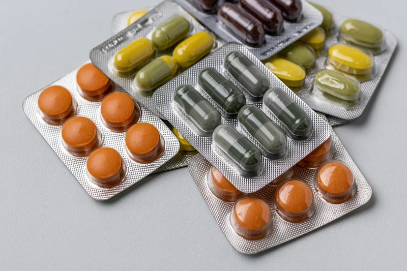Multiple blister packs of assorted pharmaceutical pills and capsules on a gray surface