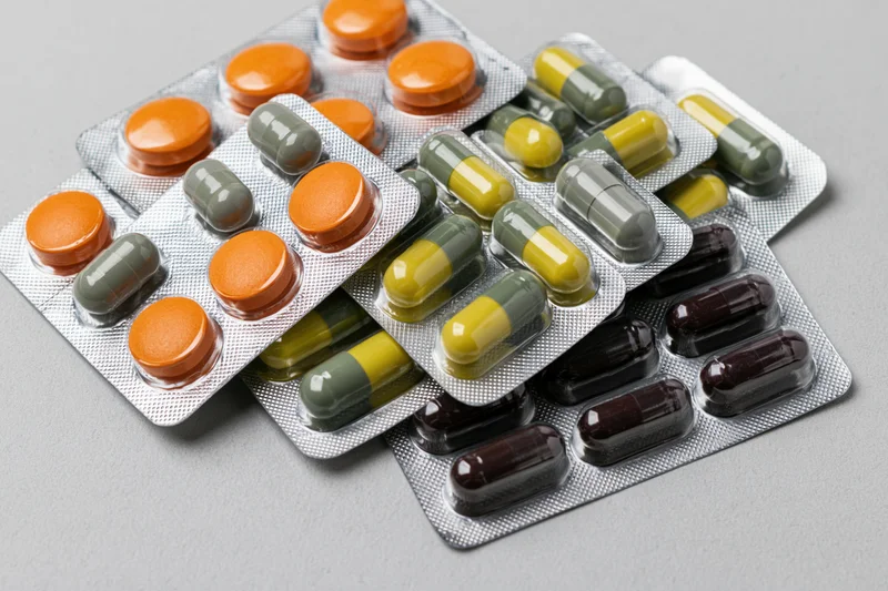 Multiple blister packs of assorted pharmaceutical pills and capsules on a gray surface