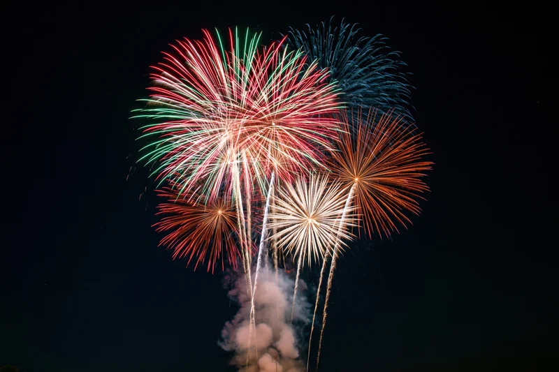 Multiple fireworks bursting simultaneously in the dark night sky