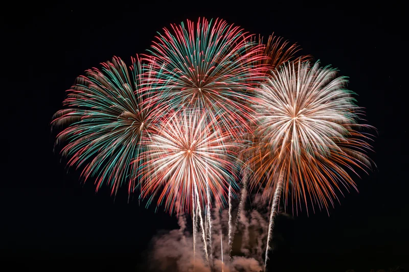 Multiple fireworks bursting simultaneously in the dark night sky