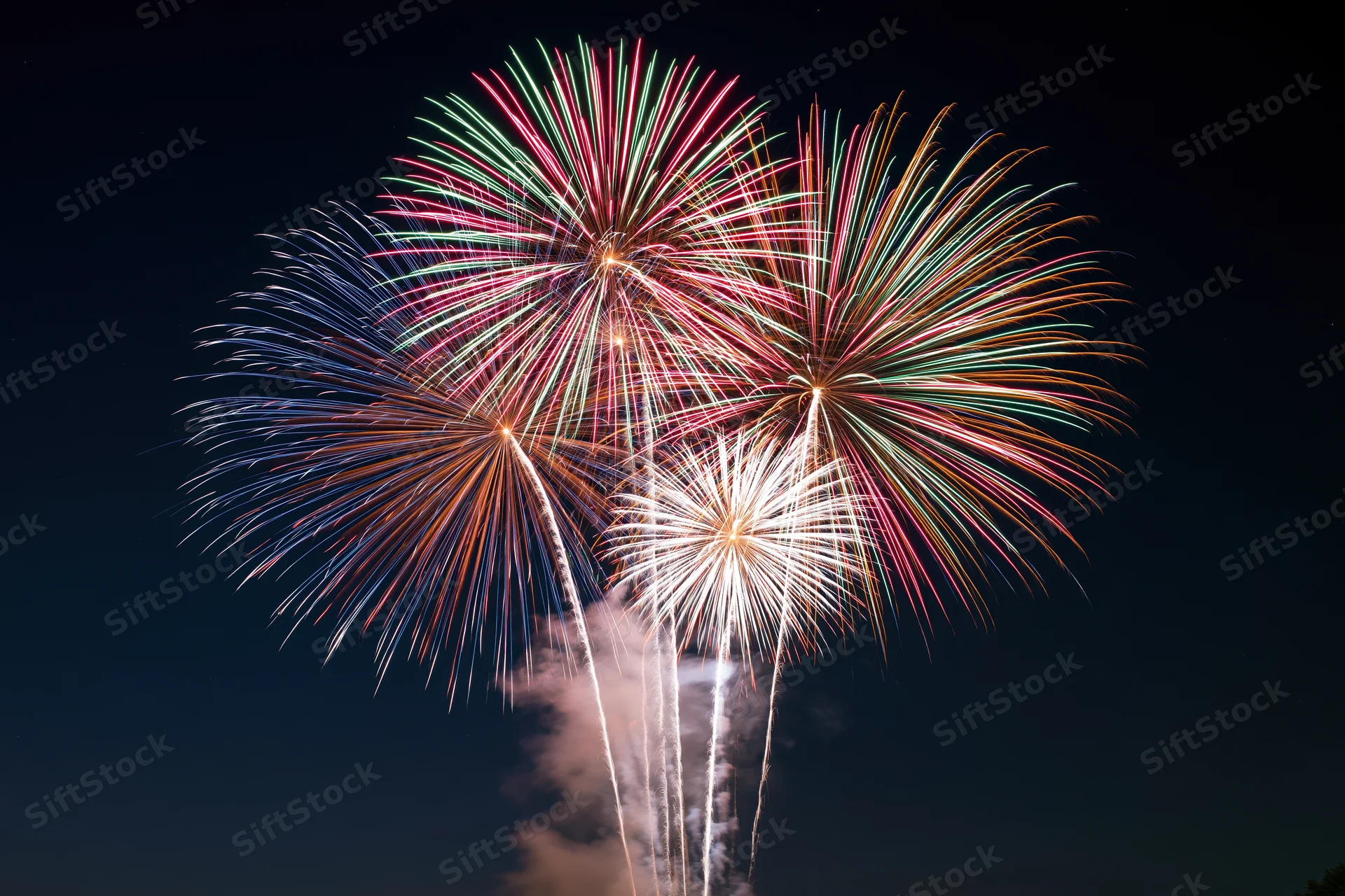 Multiple fireworks bursting simultaneously in the dark night sky