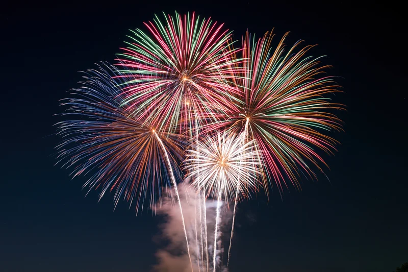 Multiple fireworks bursting simultaneously in the dark night sky
