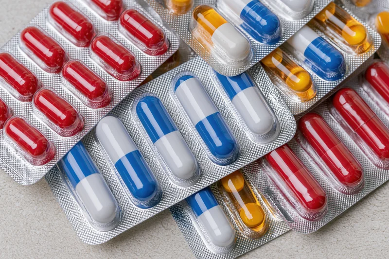 Overlapping pharmaceutical blister packs with red, blue, white and yellow capsules on a light surface