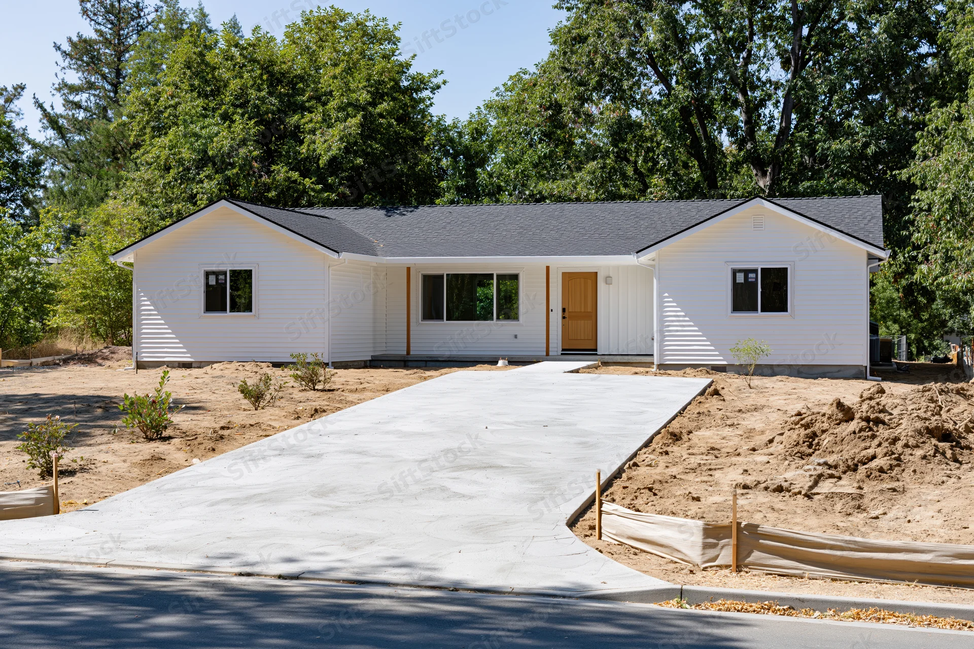 Newly poured concrete driveway leading to a single-story white house with landscaping and trees around