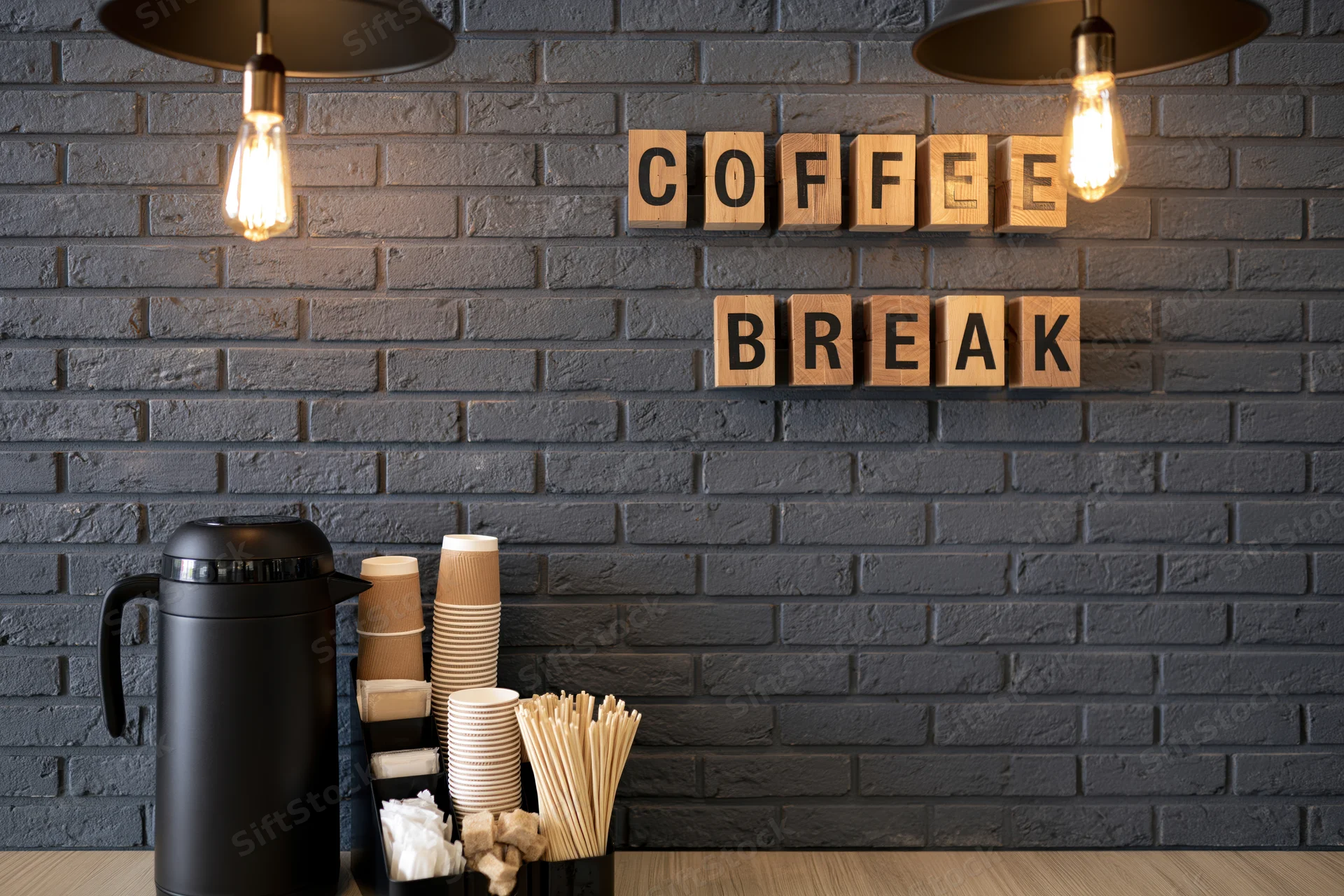 Coffee break station with wooden letter blocks on dark grey brick wall in office interior