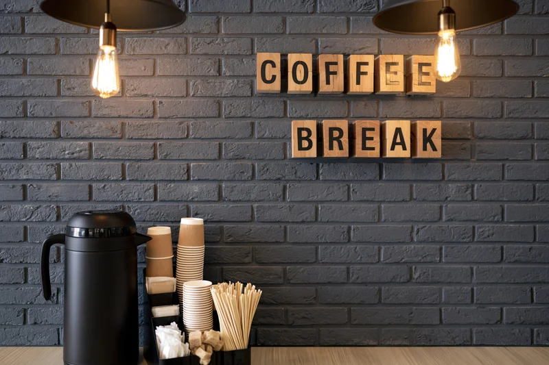 Coffee break station with wooden letter blocks on dark grey brick wall in office interior