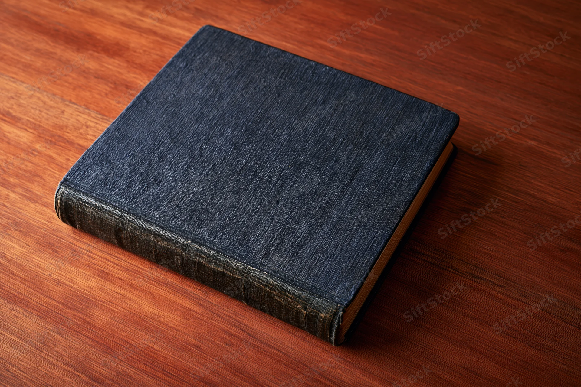 Old worn hardcover book with dark navy textured cloth cover resting on wooden table surface