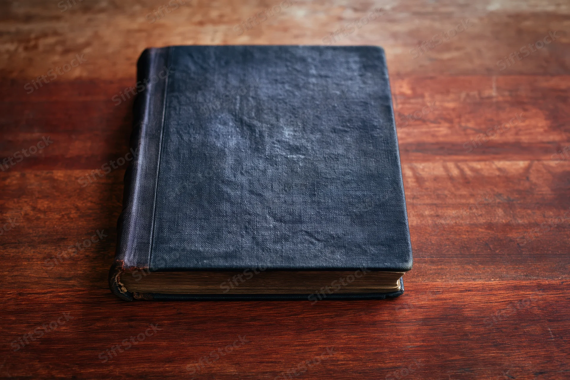 Old worn hardcover book with dark navy textured cover resting on wooden table