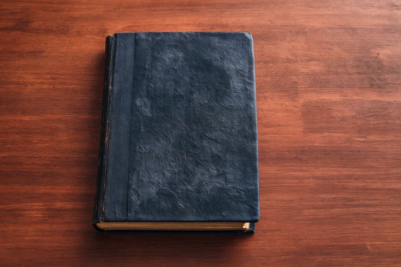 Old worn hardcover book with dark navy textured cover resting on wooden table