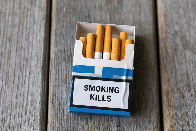 Open cigarette pack with smoking kills warning label on wooden surface