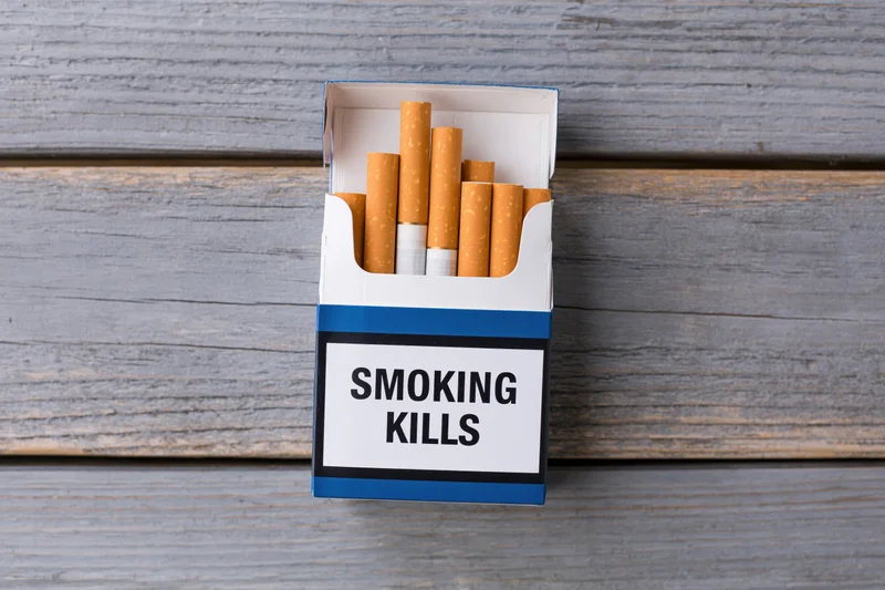 Open cigarette pack with smoking kills health warning label on wooden surface
