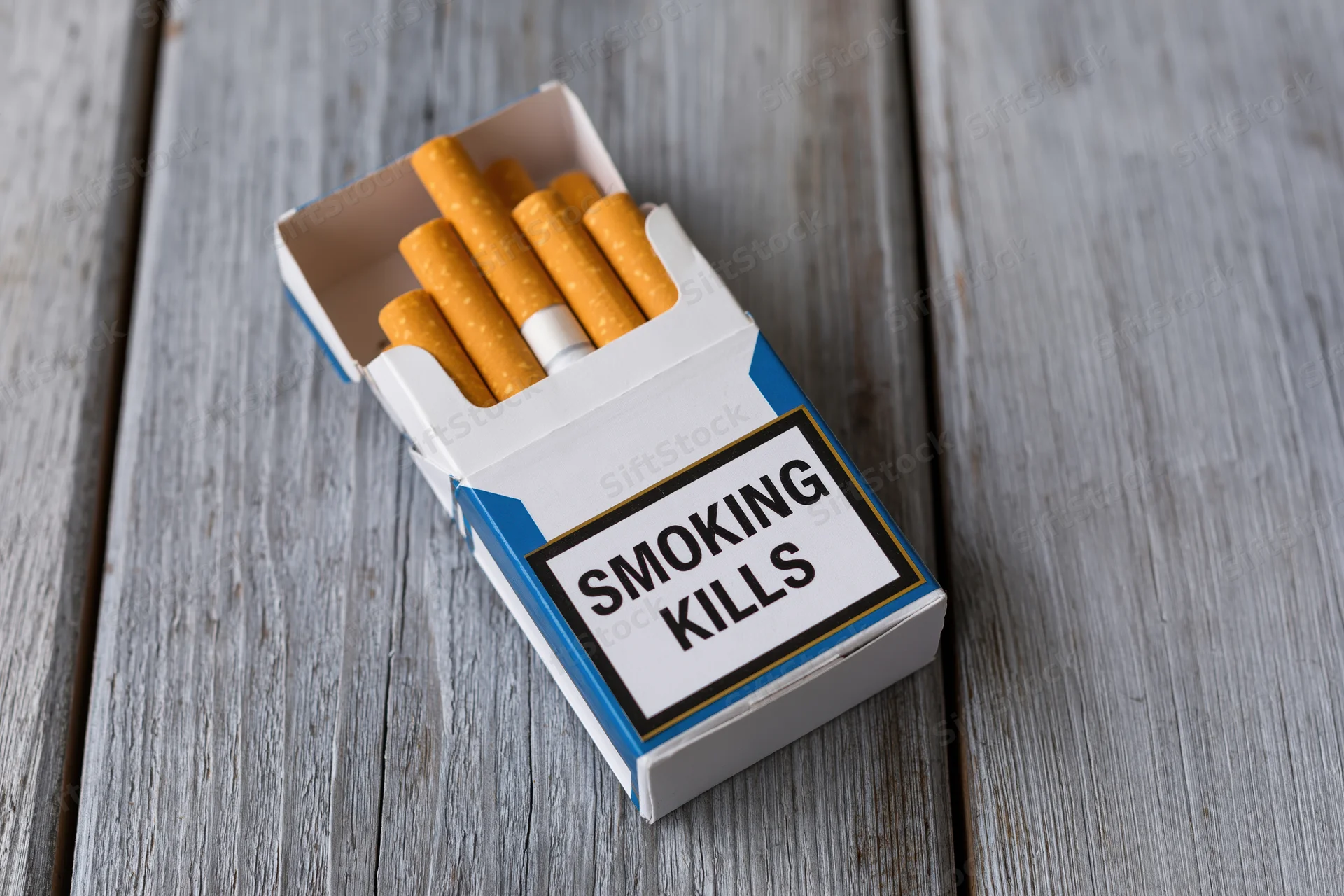 Open cigarette pack with smoking kills warning label on wooden surface