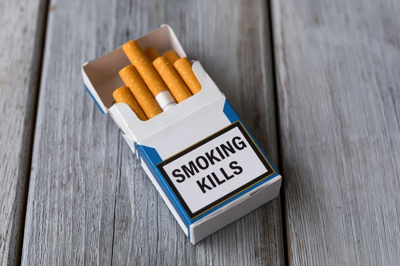 Open cigarette pack with smoking kills warning label on wooden surface